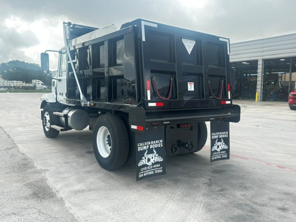 Dump truck rear-view showing dump bed and mud flaps with sponsor logos, undercarriage, rear tires, and trailer hitch area.