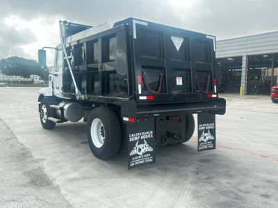 Dump truck rear-view showing dump bed and mud flaps with sponsor logos, undercarriage, rear tires, and trailer hitch area.