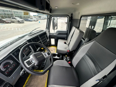 Cab interior of a 2027 Mack MD7 dump truck showing steering wheel, dashboard, driver seat, passenger seat, and center console with cup holders.