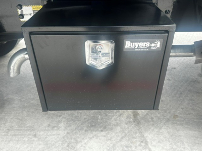 Rectangular black storage toolbox under a Mack MD7 truck showing a silver lock and a Buyers label on the front.