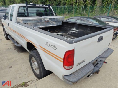 Ford F-350 pickup truck bed and rear quarter with 4x4 badge, white with orange side decals, extended cab, utility toolbox in bed, rear bumper and tail light visible.