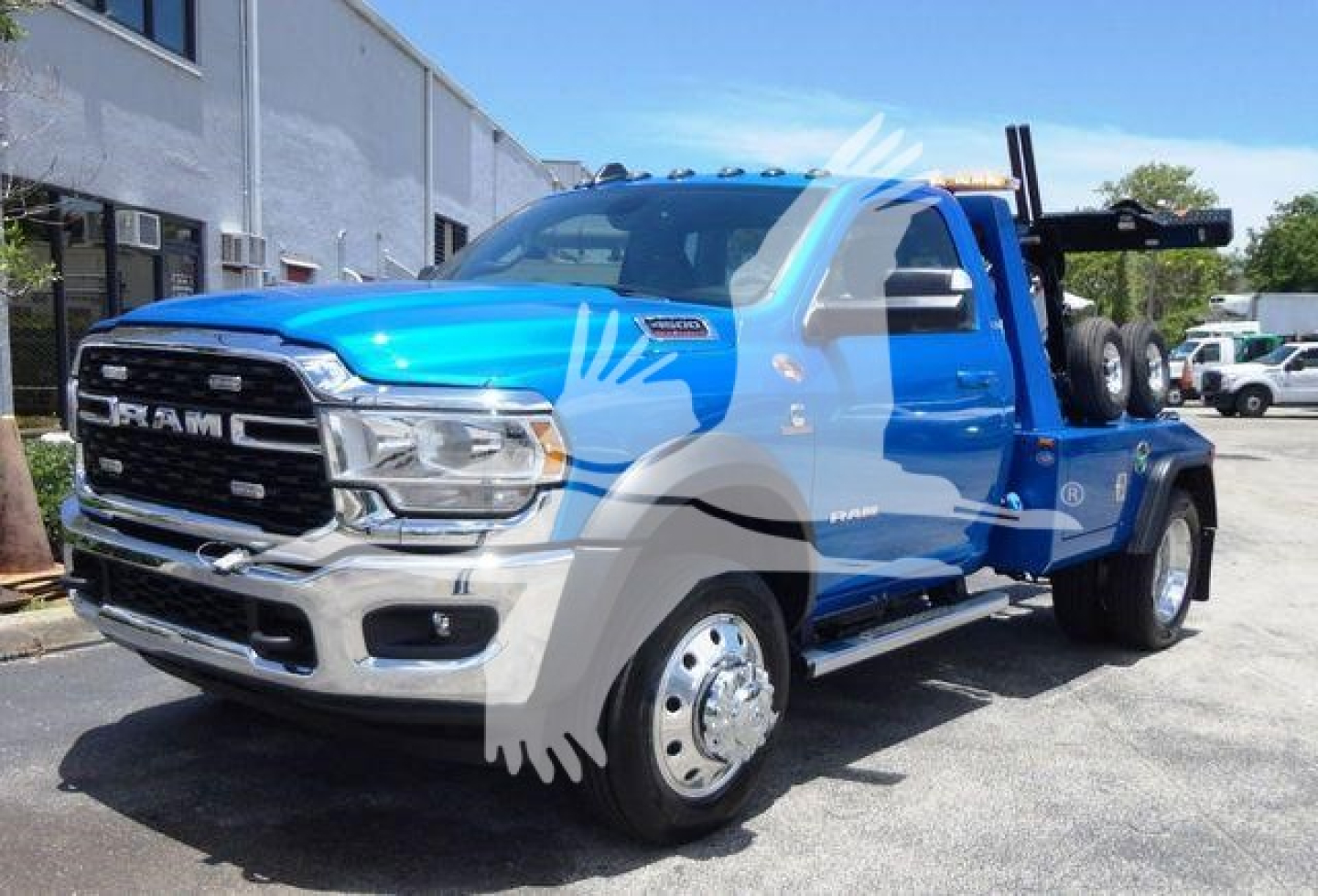 Ram 4500 tow truck in blue with graphic wrap, front grille, wheels, and winch bed visible.