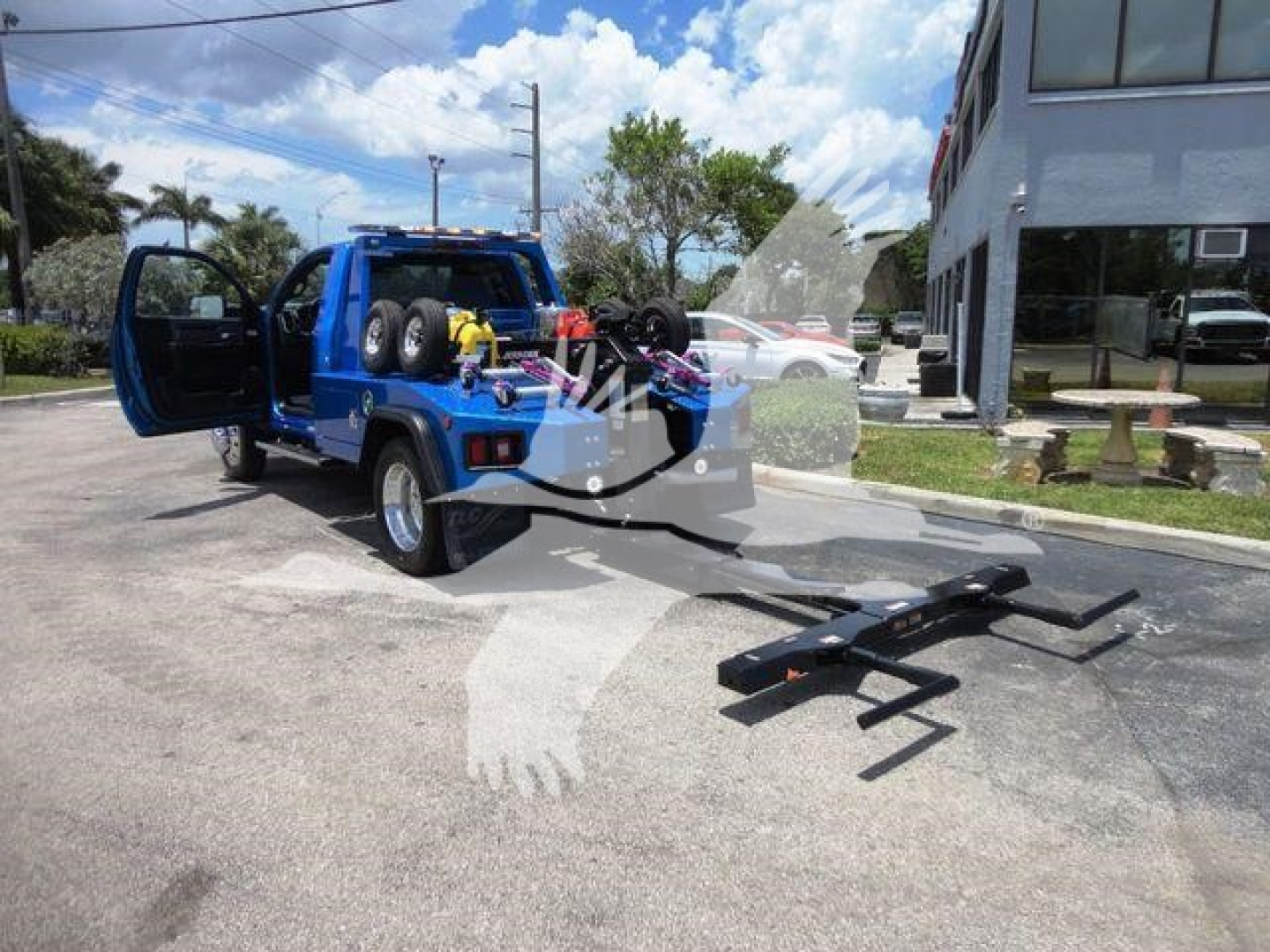 Ram 4500 SLT truck with doors open showing winch equipment and tow bar in bed, blue vehicle, black ramp on ground.