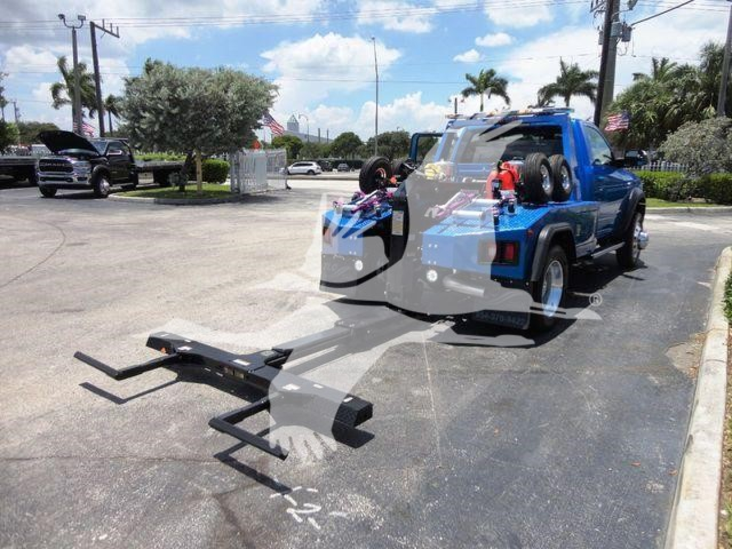 Blue Ram 4500 pickup with winch attachment on rear, truck bed mounted equipment, side profile in a dealership lot.