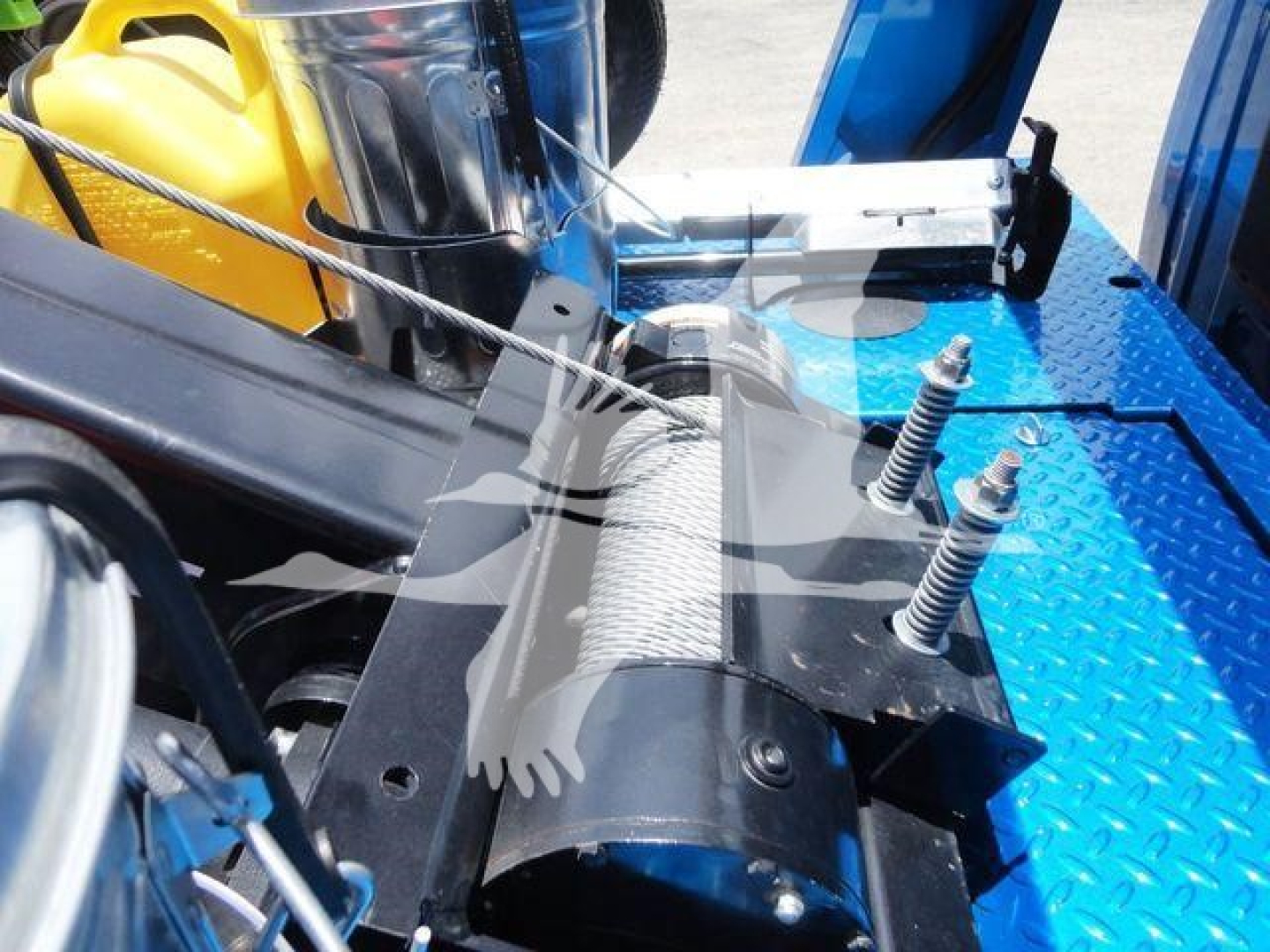 Winch assembly mounted on blue truck bed with hydraulic line and stainless steel cable, showing winch drum and mounting brackets.