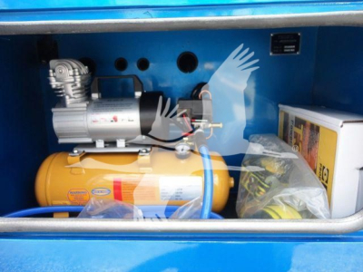 Winch assembly and yellow air tank inside blue truck bed compartment showing electric motor and hydraulic components.