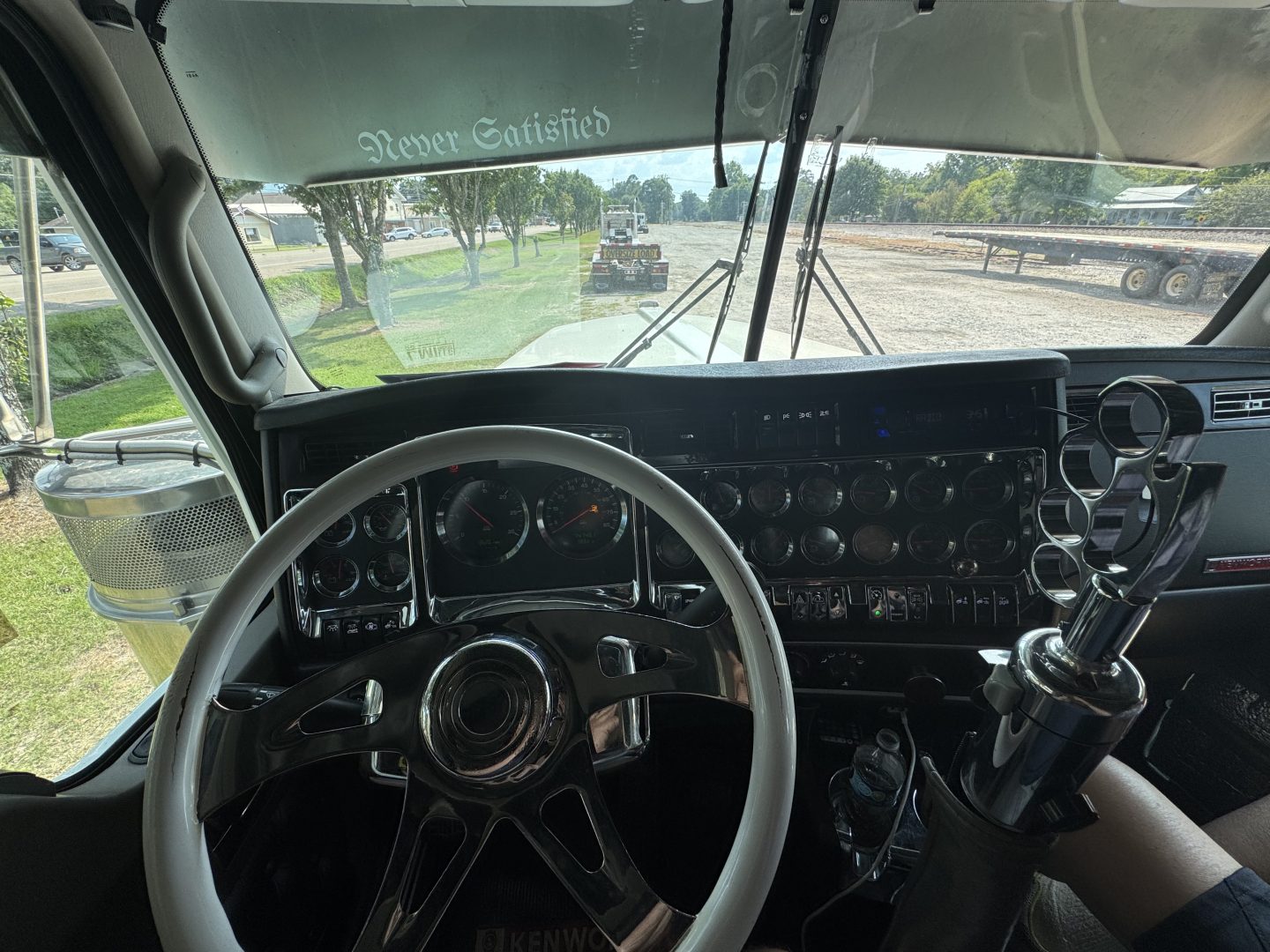 Kenworth W900L interior view showing steering wheel, dashboard with gauges, transmission shifter, and large instrument cluster