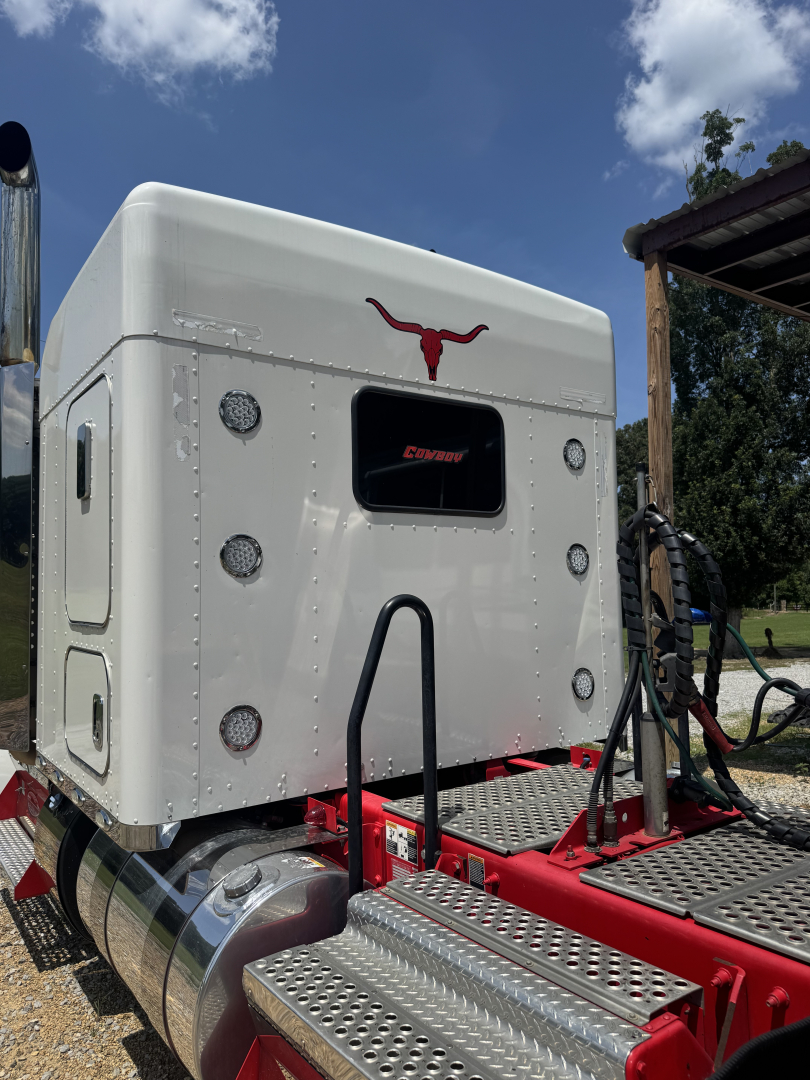 Kenworth W900L sleeper cab with white exterior, front view showing red torque bull logo and rear access steps.