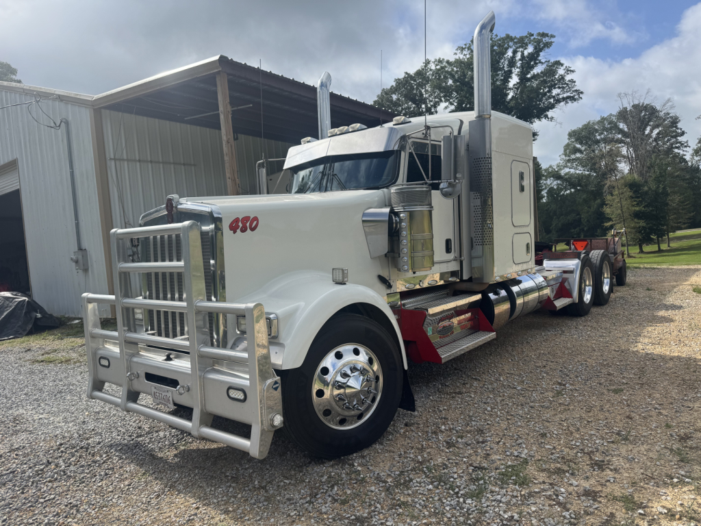 Kenworth W900L conventional sleeper truck showing chrome grille guard and dual chrome exhaust stacks.