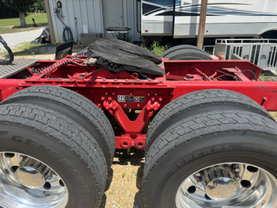 Kenworth W900L chassis near rear showing dual rear axles, tires, and red frame with exposed components.
