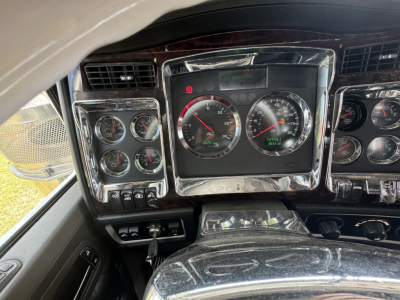 Dashboard of a 2023 Kenworth W900L conventional sleeper showing analog gauge cluster with chrome surrounds and woodgrain trim.