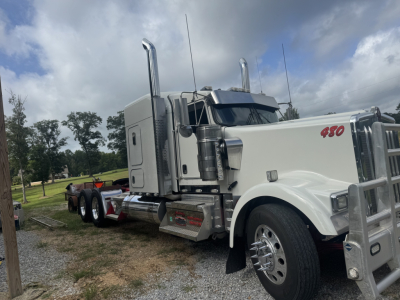 Kenworth W900L conventional sleeper truck from a front-right-angle view showing its chrome exhaust stacks, white cab with red '450' badge, and dual rear axles.