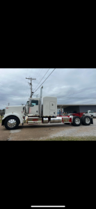 Kenworth W900L conventional sleeper truck side view showing long cab, dual rear axles, chrome exhaust stacks, and white/cream color.