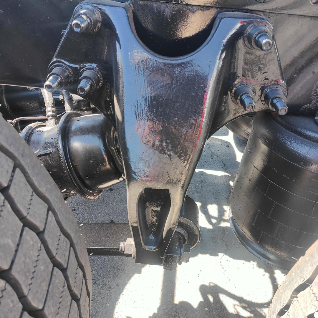 View of truck front suspension showing main leaf spring bracket, U-bolts, air lines, and shock absorber mounts under a 2021 International LT truck.