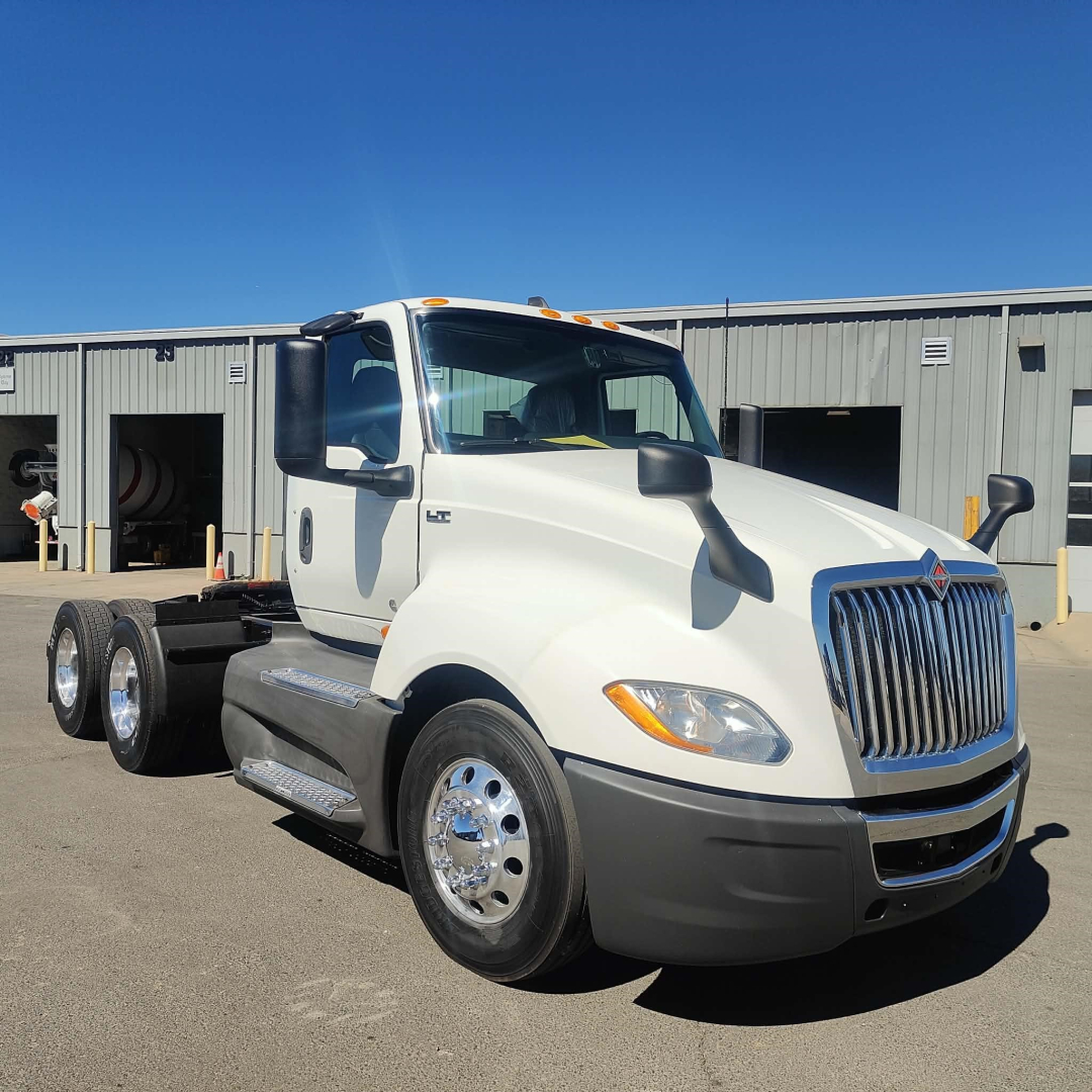 International LT conventional daycab truck in white, front-right view, chrome grille, dual rear axles, with side steps and large mirrors.