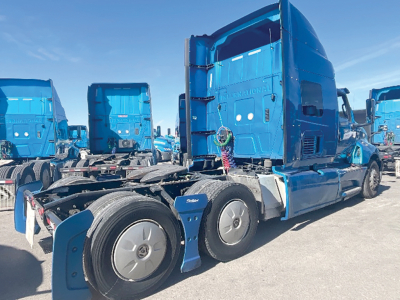 Semi truck cab and chassis in blue with sleeper, side view showing International logo on rear door.
