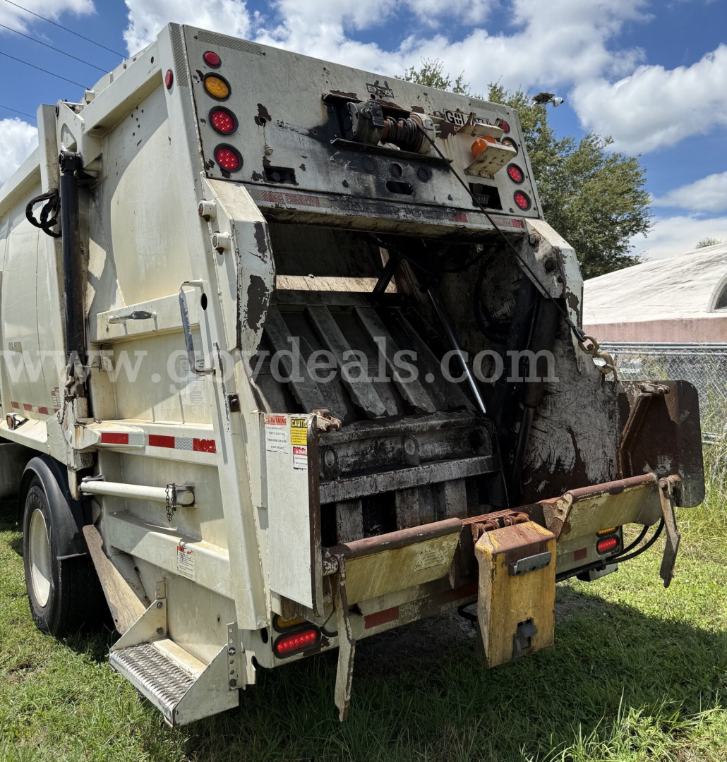 Rear view of a 2015 Hino garbage truck with hydraulic compactor, showing worn hopper interior and load chute, taillights, hoses, and side steps.
