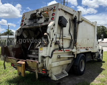 Rear/side view of a 2015 Hino 338 garbage truck showing rear compactor and hydraulic systems, white body with metal components and taillights.