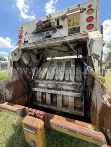 Rear view of a 2015 Hino 338 waste collection truck showing hydraulic compactor mechanism, hydraulic hoses, and tailgate area with worn metal surfaces and rust highlights.