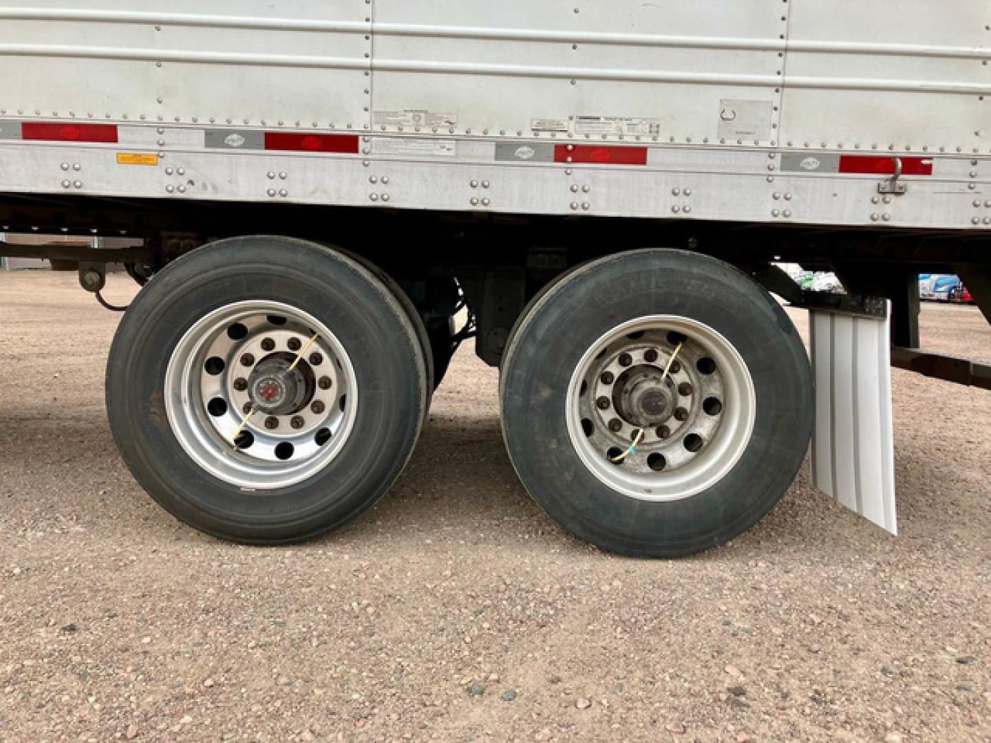 Trailer wheel axles of a refrigerated utility trailer showing dual rear rims and tires under a metal sidewall.