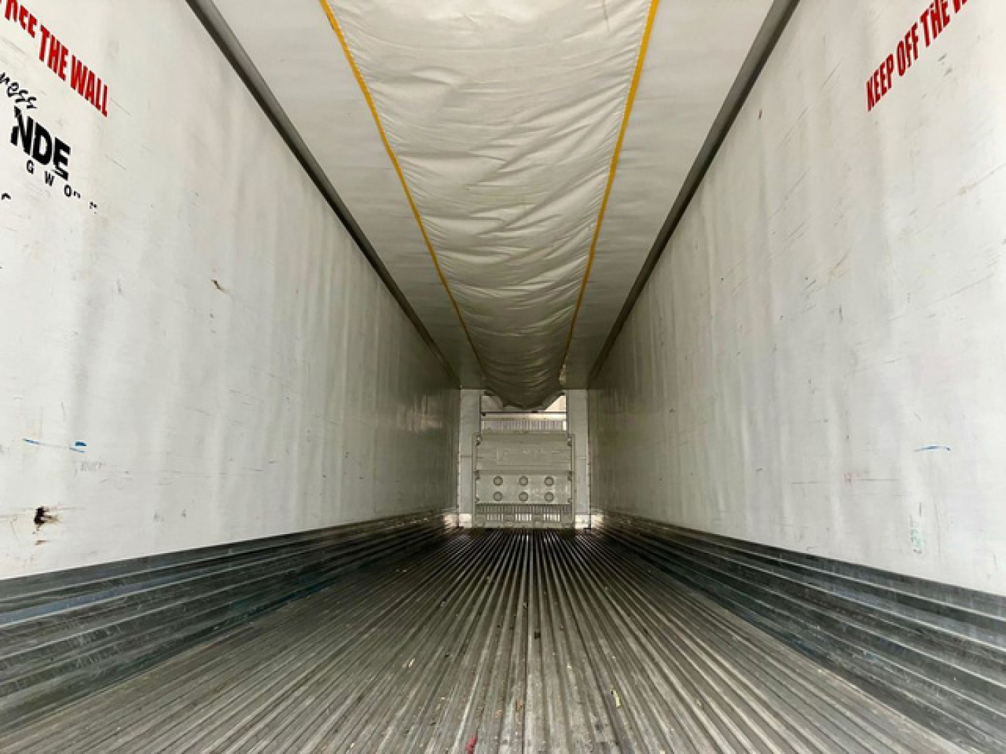 Trailer interior showing long refrigerated cargo area with ribbed floor and white sidewalls, yellow ceiling stripe, rear doors at far end.