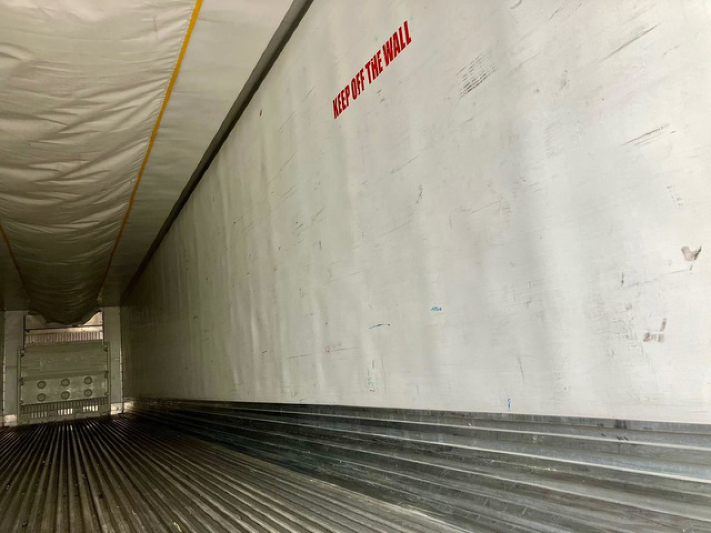 Trailer interior showing longitudinal ribbed floor and insulated wall with warning text 'KEEP OFF THE WALL' in view.