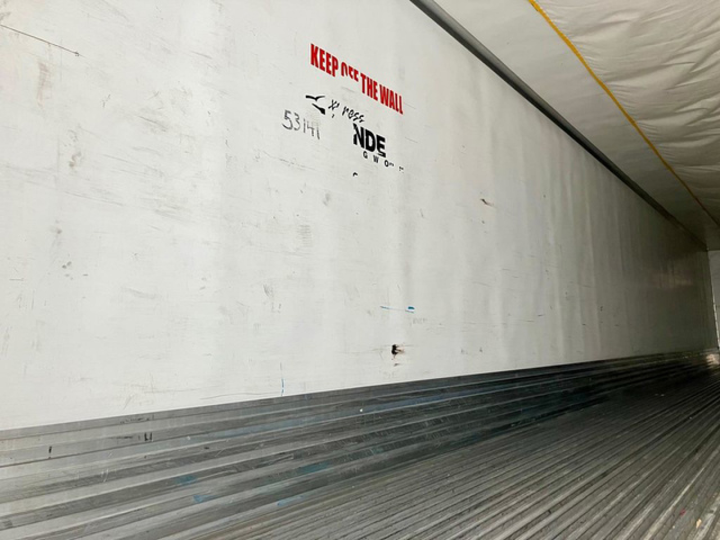 Trailer interior wall with white surface and ribbed floor showing a Refrigirated trailer branding and 'KEEP OUT THE WALL' text.