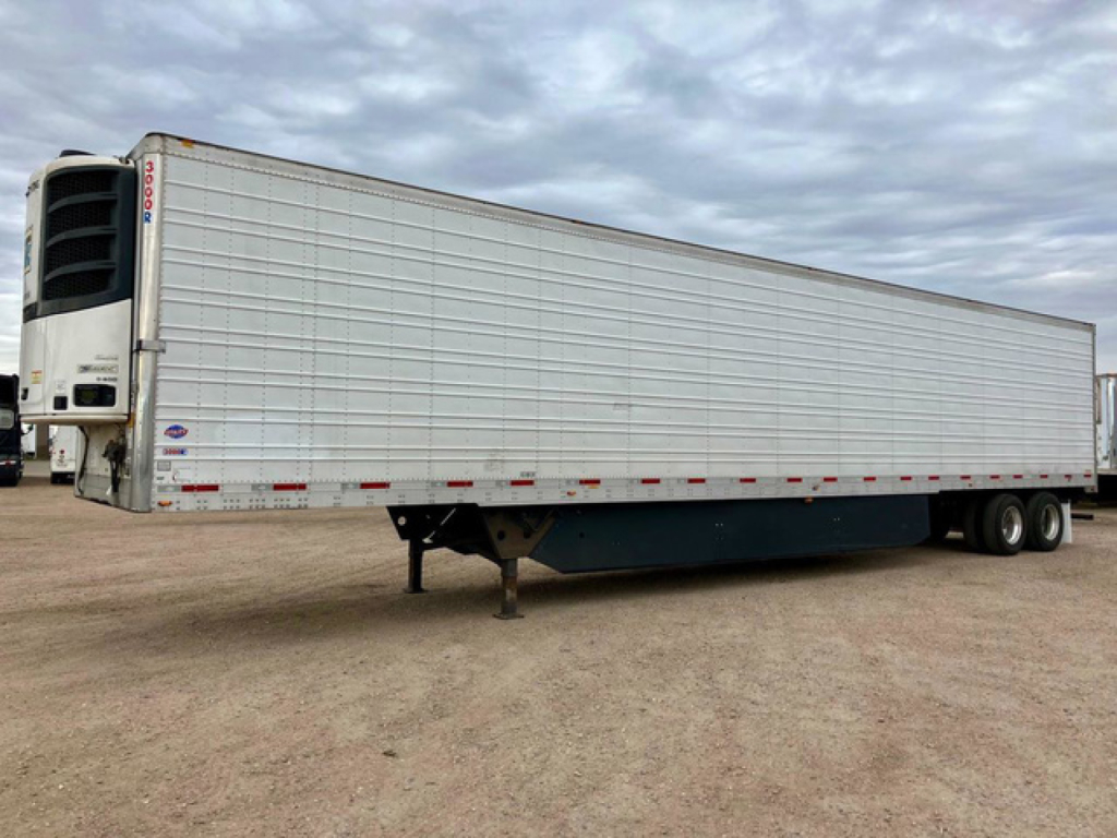 Refrigerated trailer side view showing box with vertical ribbed panels and rear refrigeration unit, undercarriage with dual rear axle and landing gear, empty lot