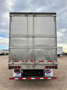 Rear view of a used 2020 Utility refrigerated trailer with diamond plate aluminum doors, multiple hinge outlines, and red/white reflective tape along bumper.
