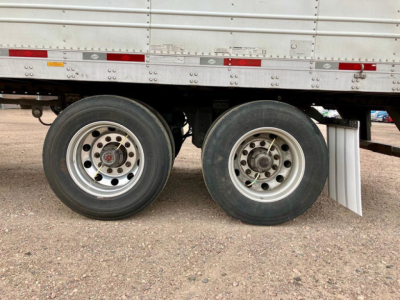 Trailer wheel axles of a refrigerated utility trailer showing dual rear rims and tires under a metal sidewall.