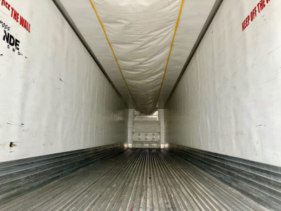 Trailer interior showing long refrigerated cargo area with ribbed floor and white sidewalls, yellow ceiling stripe, rear doors at far end.