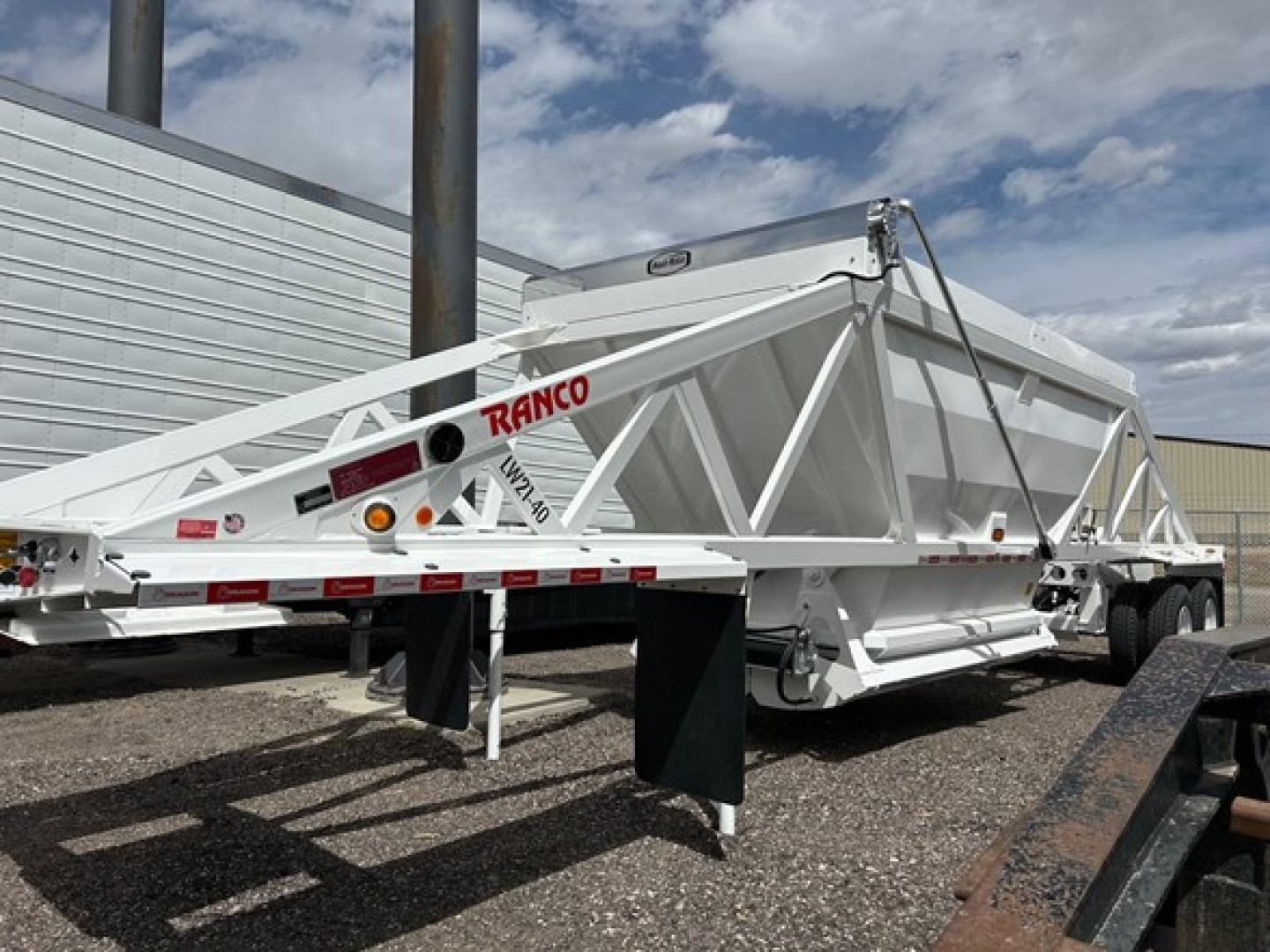 Ranco air ride bottom dump trailer in white, dual-axle with frame braces and hydraulic lift arms visible, side ramp support, brand name ‘RANCO’ on the frame.