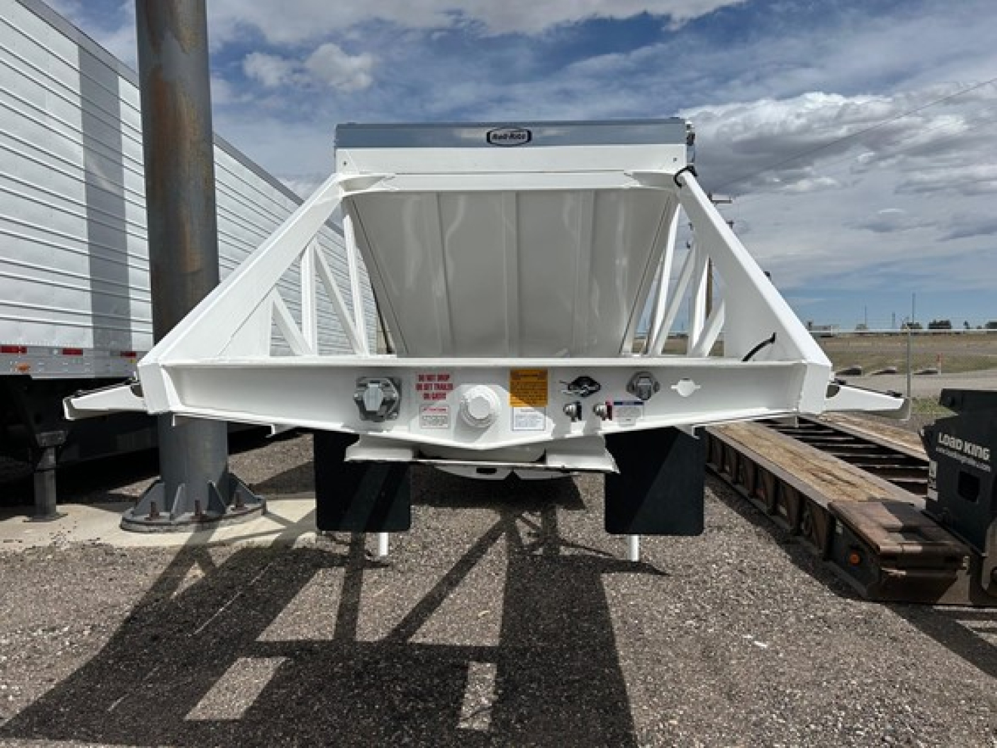 Ranco air ride bottom dump trailer viewed from rear showing white steel frame, hydraulic components, and bumper/lighting area.