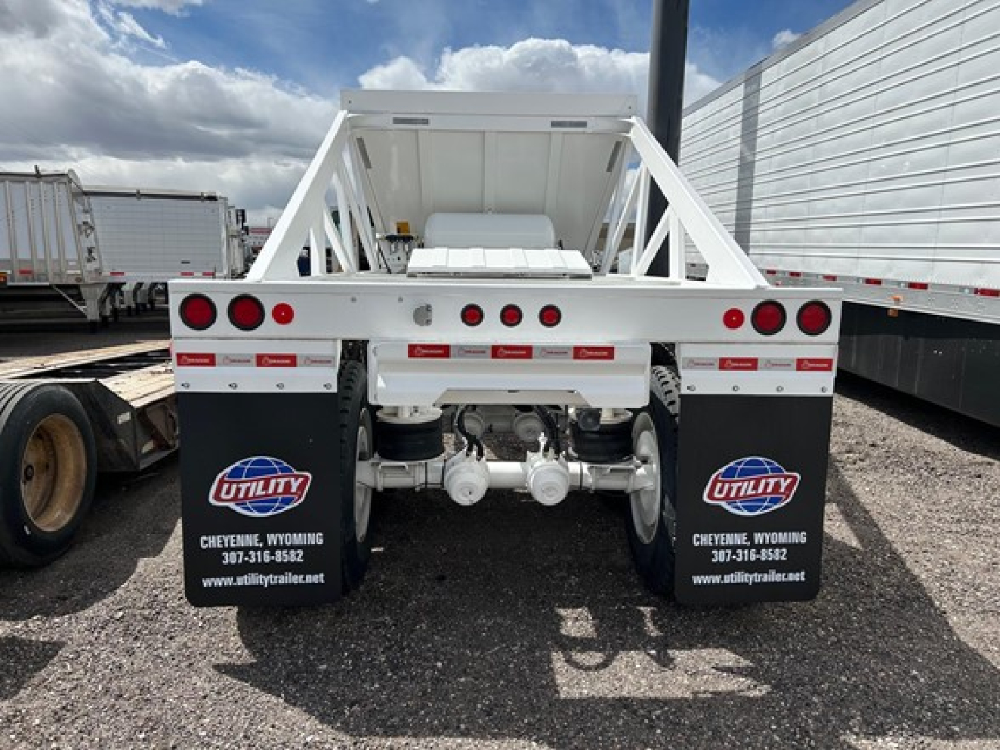Dump trailer back view showing dual rear axles and white frame with safety rails, Mudflaps with Utility branding, warning lights, and hydraulic mechanism.