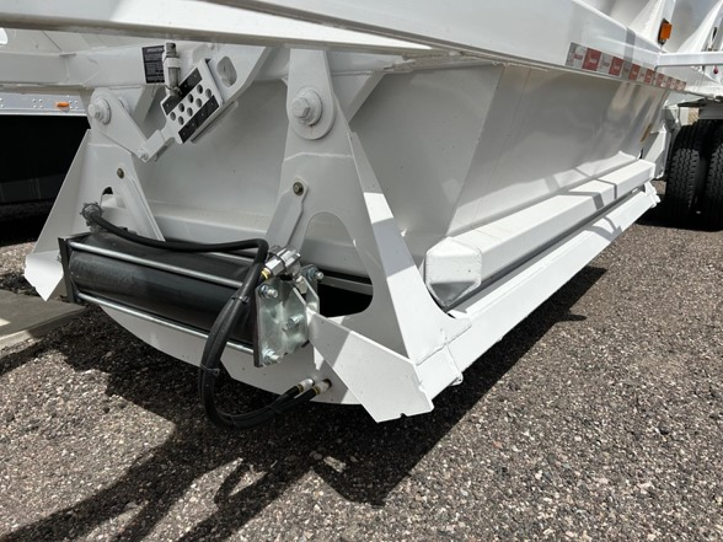 Ranco Air Ride Bottom Dump trailer lower corner with hydraulic cylinder and wiring harness visible, white metal frame and support braces.