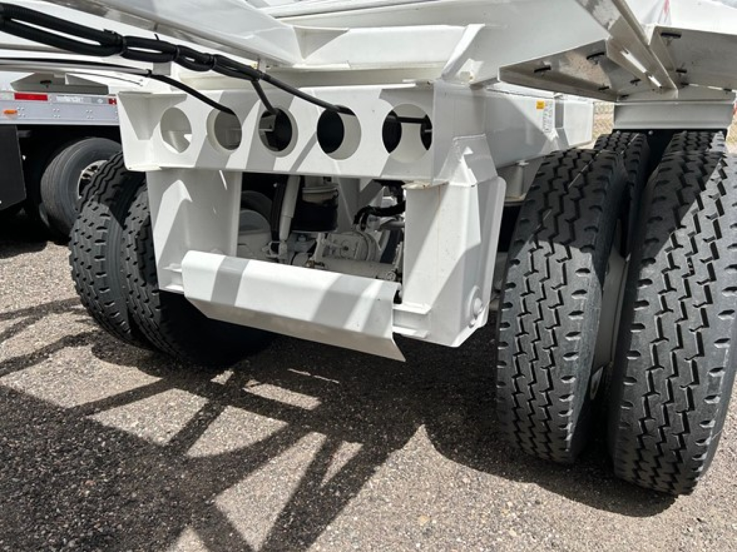 Ranco air ride bottom dump trailer undercarriage with multiple axles showing white steel frame, circular perforations, and heavy-duty wheels.