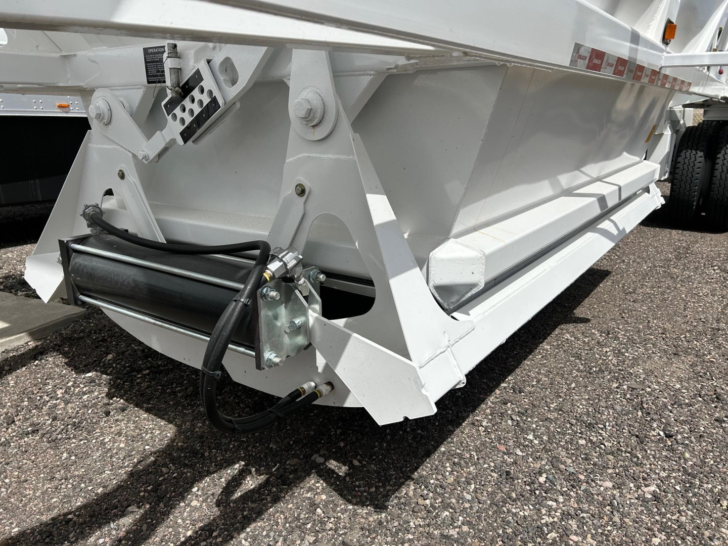 Ranco bottom dump trailer hitch area showing hydraulic cylinder and wiring harness, white painted frame, structural supports, and wheel in background.