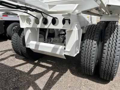 Ranco air ride bottom dump trailer undercarriage with multiple axles showing white steel frame, circular perforations, and heavy-duty wheels.