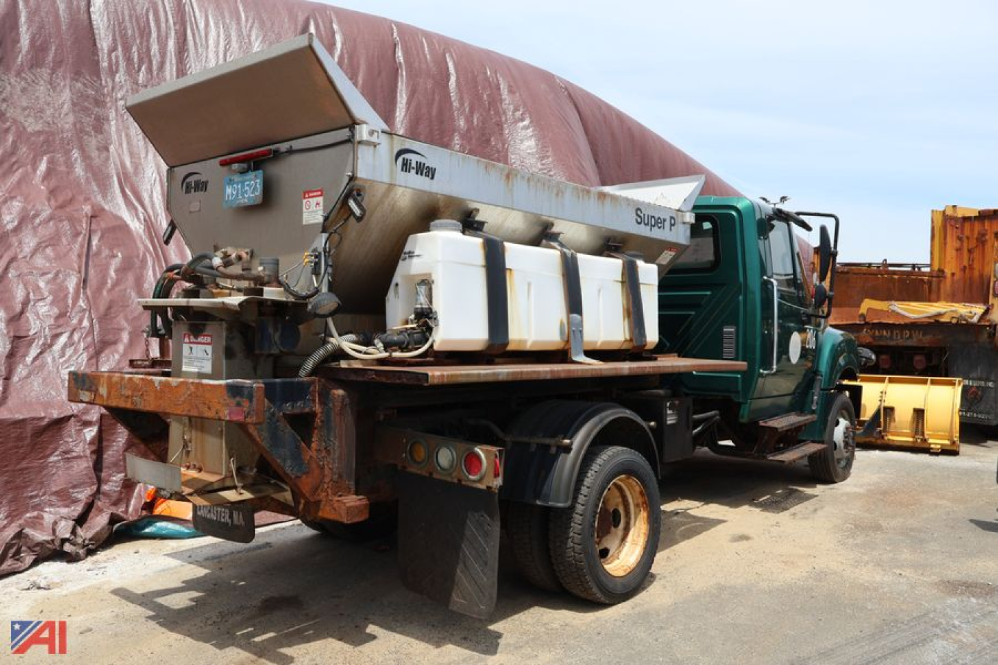 Truck with a swaploader system mounted on the chassis; large metal hopper and hydraulic lines visible; International TerraStar medium-duty truck in green; equipment trailer and yard behind.