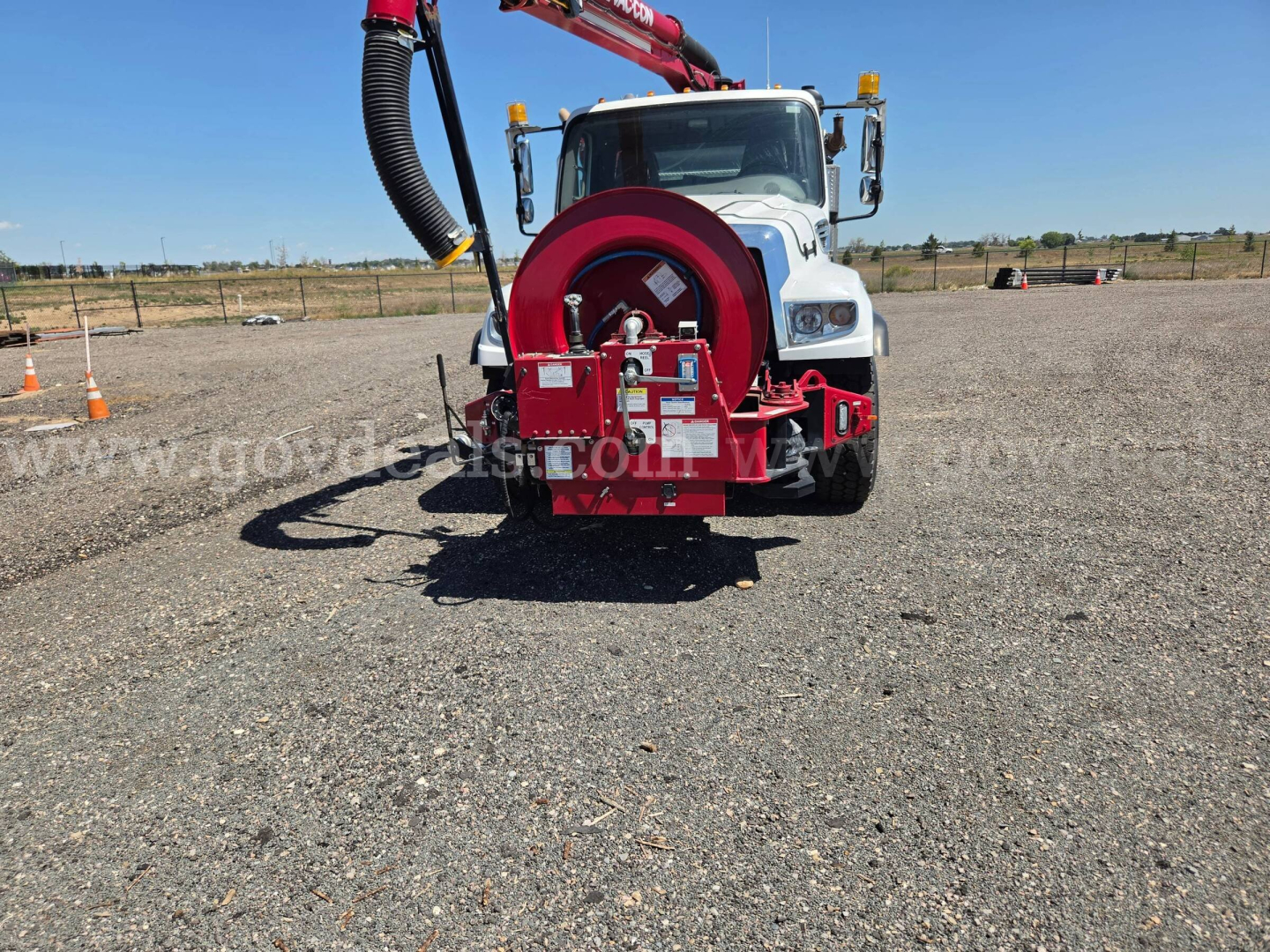 Front view of a white Freightliner 114SD vacuum truck with a red hose reel and hose on the back, in an open lot.