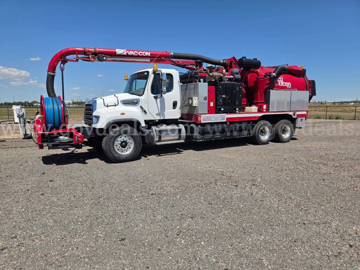 Vacuum truck with white cab and red rear equipment, long hose reel on side, Freightliner 114SD chassis