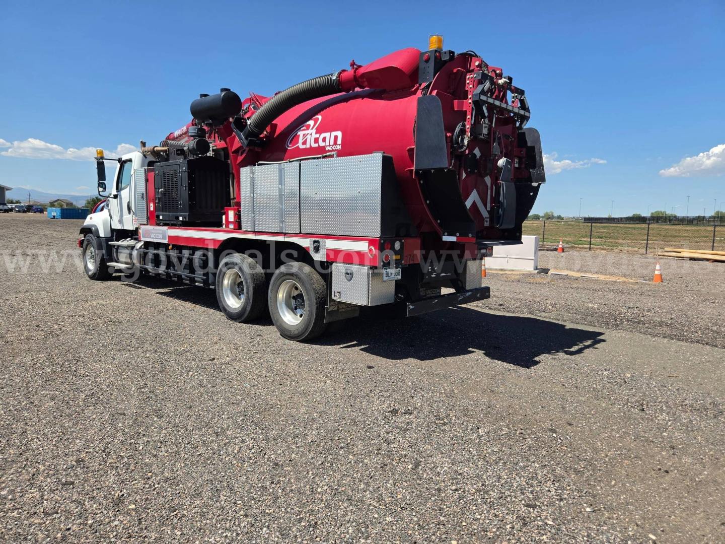 Freightliner vacuum truck side and rear view with red tanker and hoses, logo visible, underclear sky.