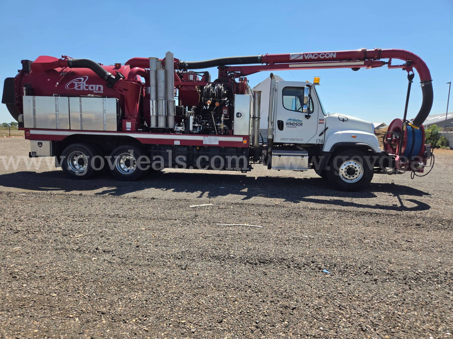 Truck-mounted vacuum pump rig with red hose reel on a white cab and chassis, side view showing equipment labels and storage compartments.
