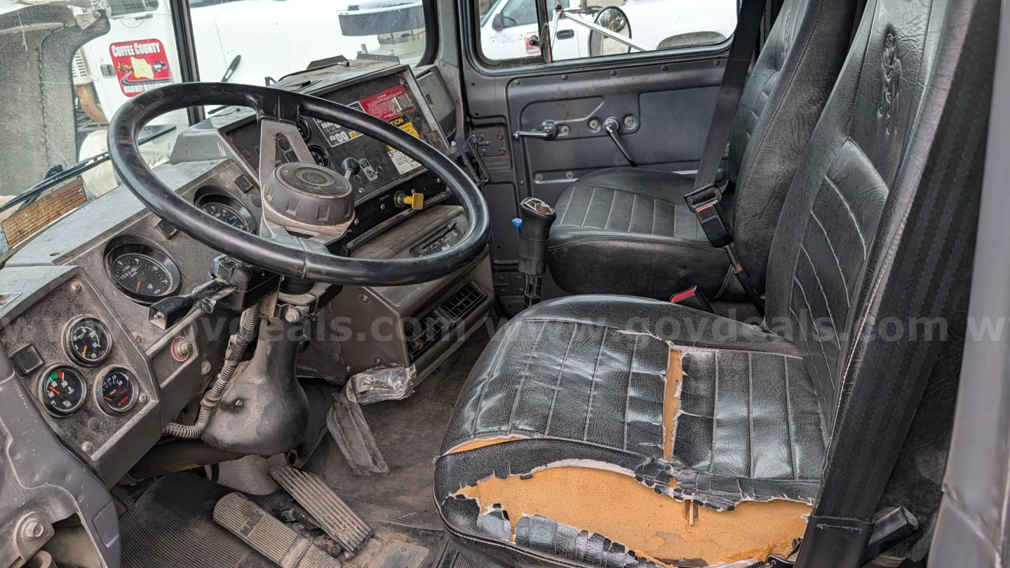 Mack RD690S cab interior showing steering wheel, dashboard gauges, and driver seat with torn upholstery.