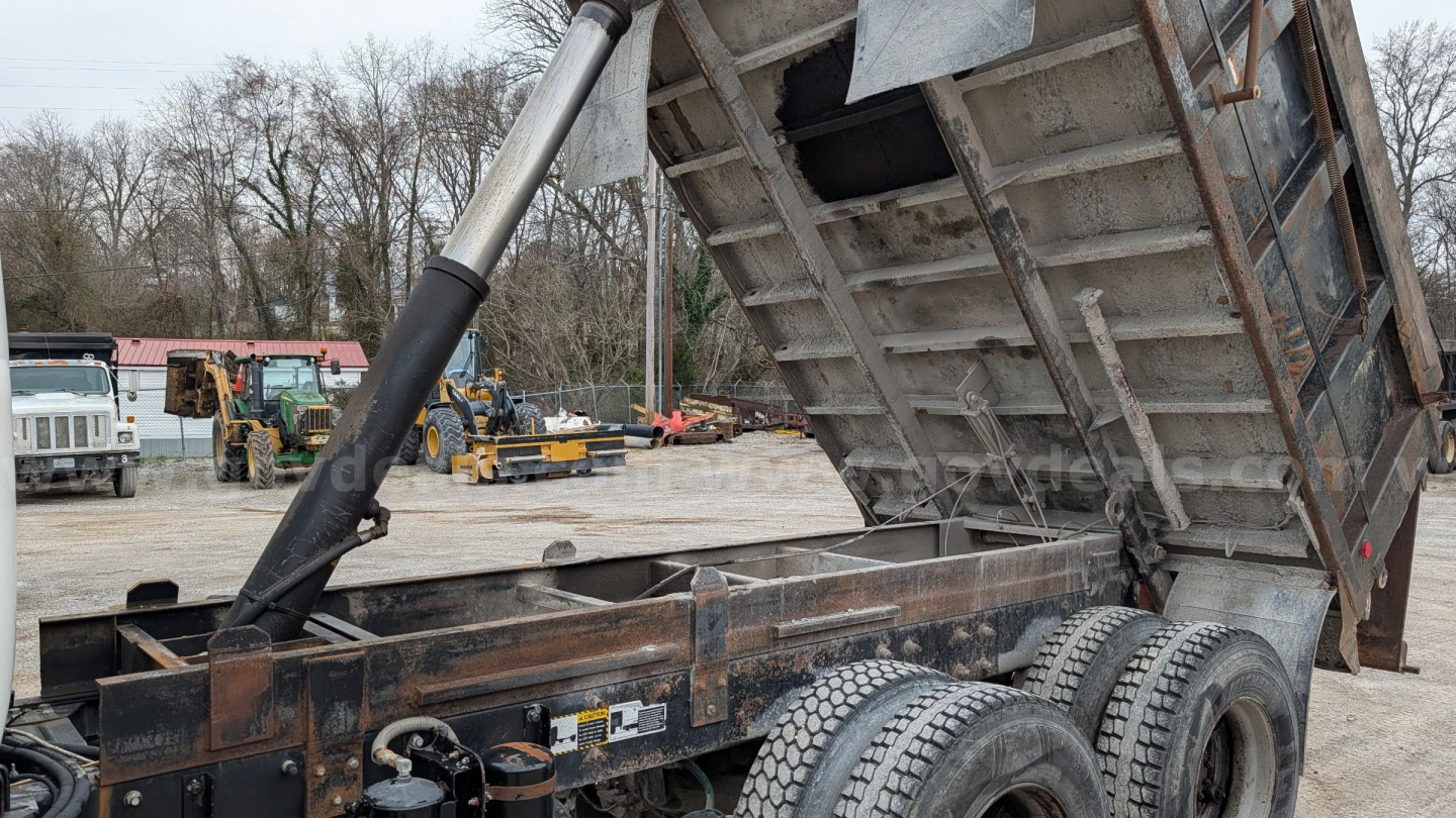 Dump truck frame showing hydraulic ram lifting a steel dump bed on a Mack RD690S chassis with dual rear axles.