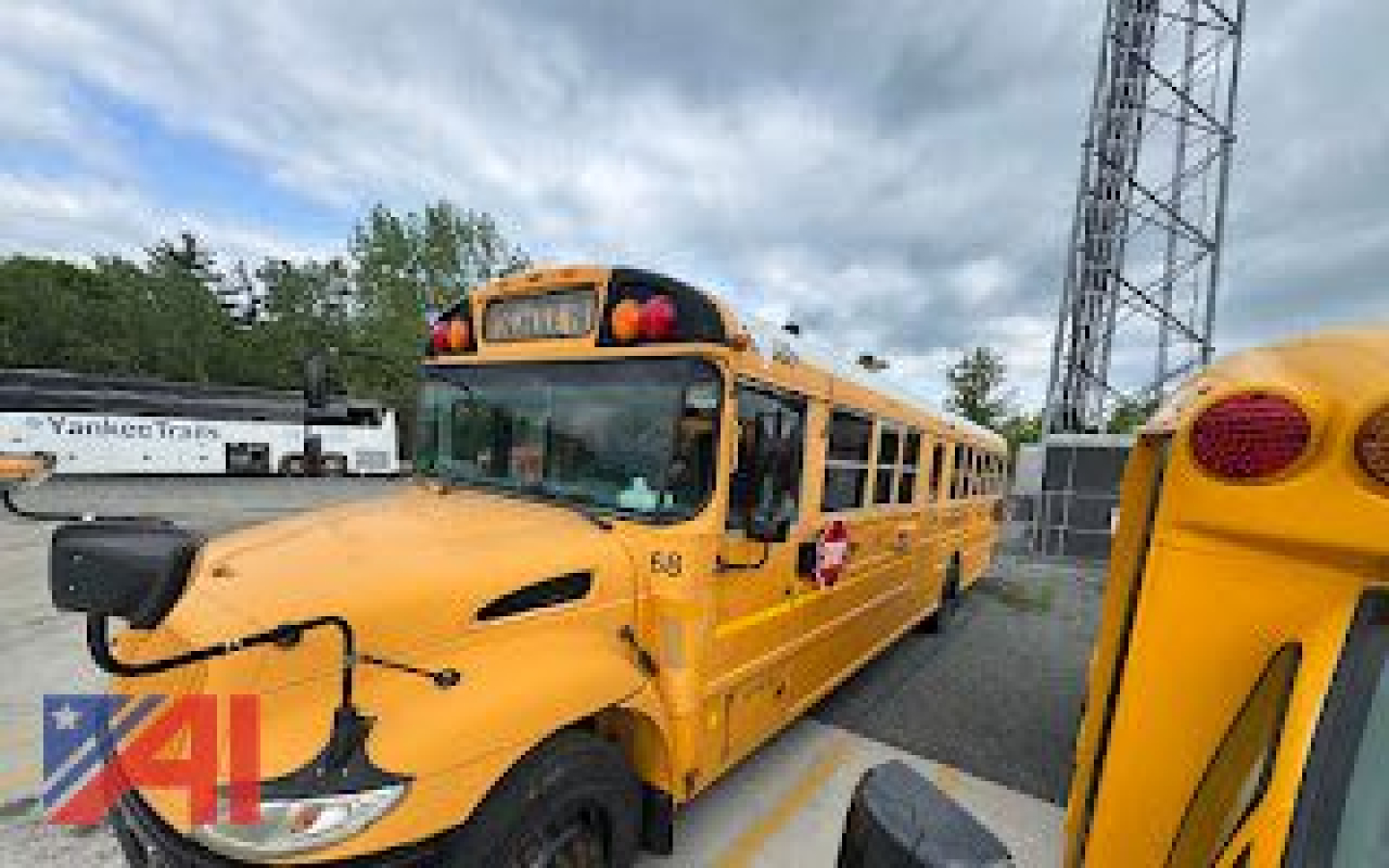School bus CE Series yellow bus parked with front hood and bumper visible, Kawasaki school bus emblem, V-shaped hood contours, roof alert lights and stop sign area.