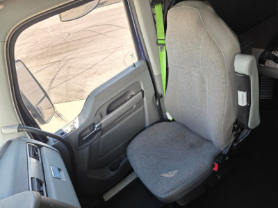 Kenworth T680 truck interior seating area view from driver door, gray cloth seat with green seatbelt, dashboard and window visible.
