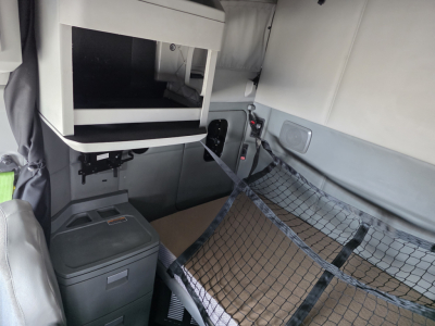 Interior of a 2018 Kenworth T680 sleeper cab showing a storage shelf, passenger seat area, and a cargo net over a mattress area.