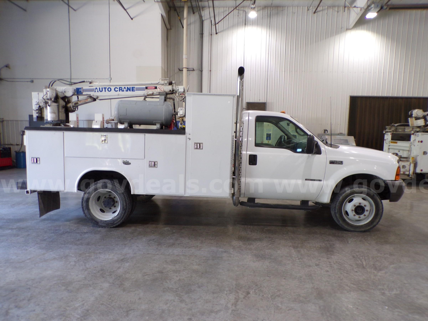 Utility service truck with bucket crane equipment mounted in service bay, white cab and utility bed showing storage compartments and rear crane unit.
