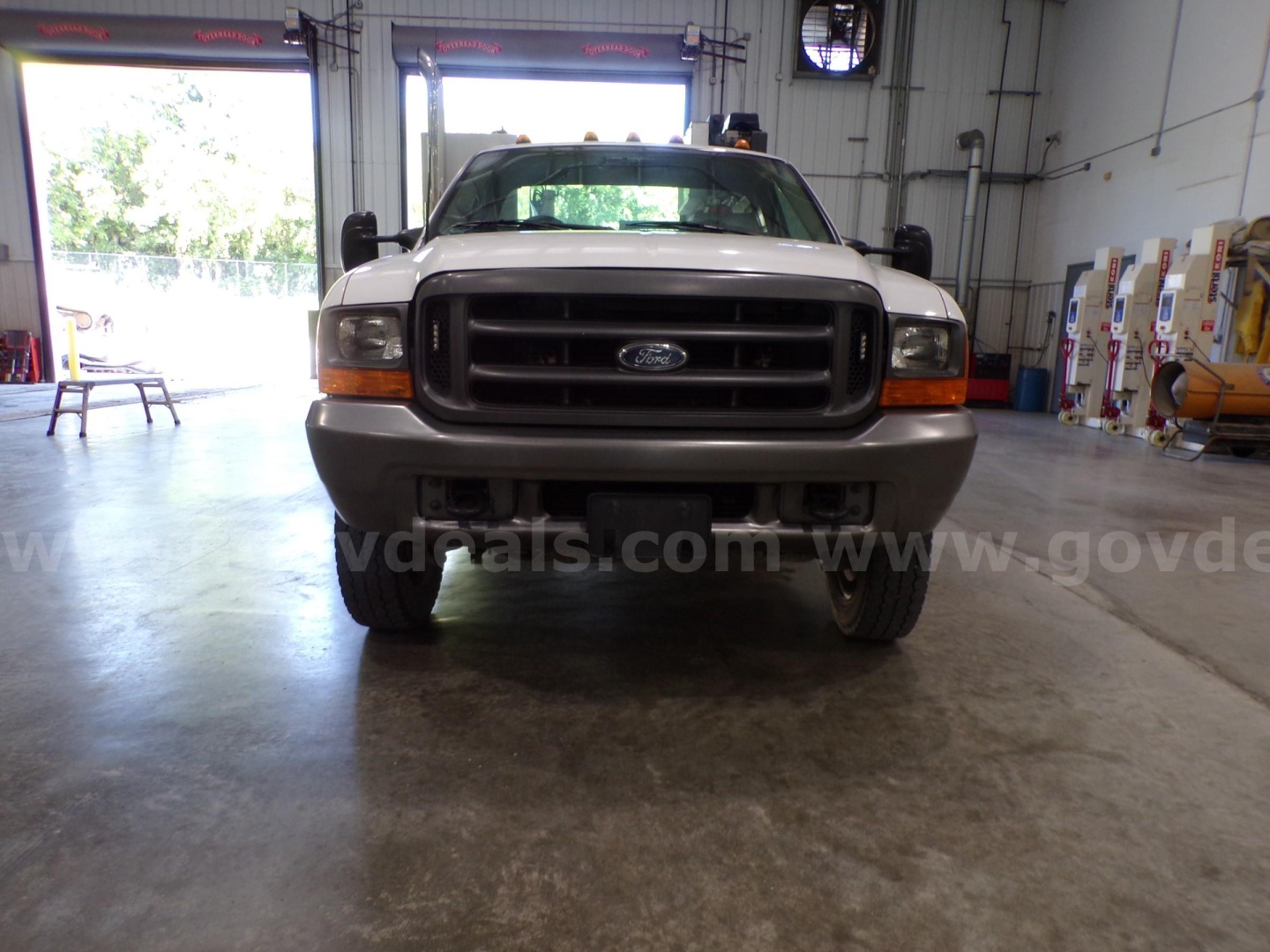 Front view of a white 2000 Ford F-450 service/utility truck in a garage with black grille, bumper, and large side mirrors.